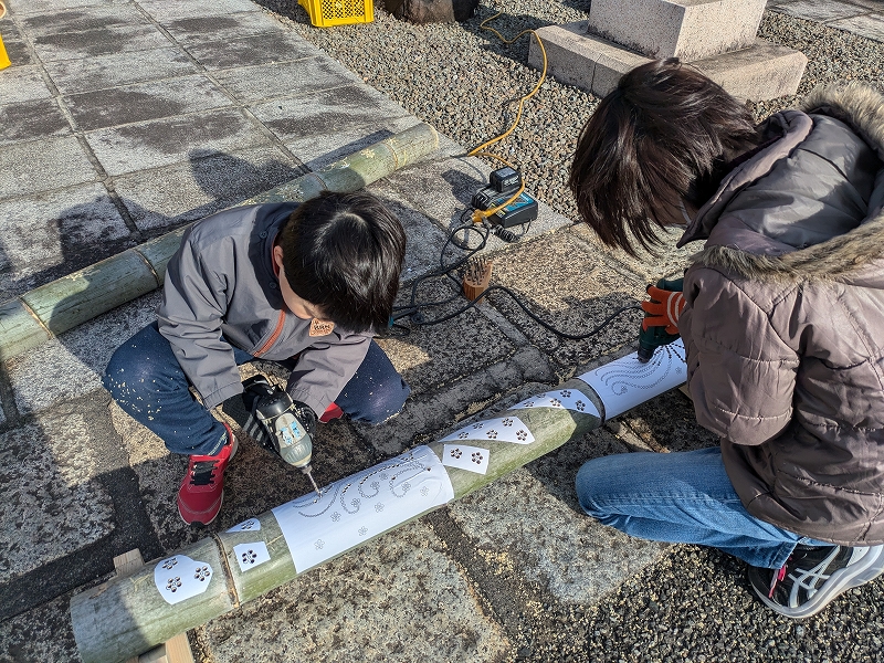 親子が竹にドリルで穴を開け、竹灯りを作っています。